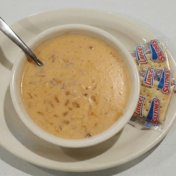 Creamy soup with a spoon in a white bowl, served with a packet of Lance Saltines.
