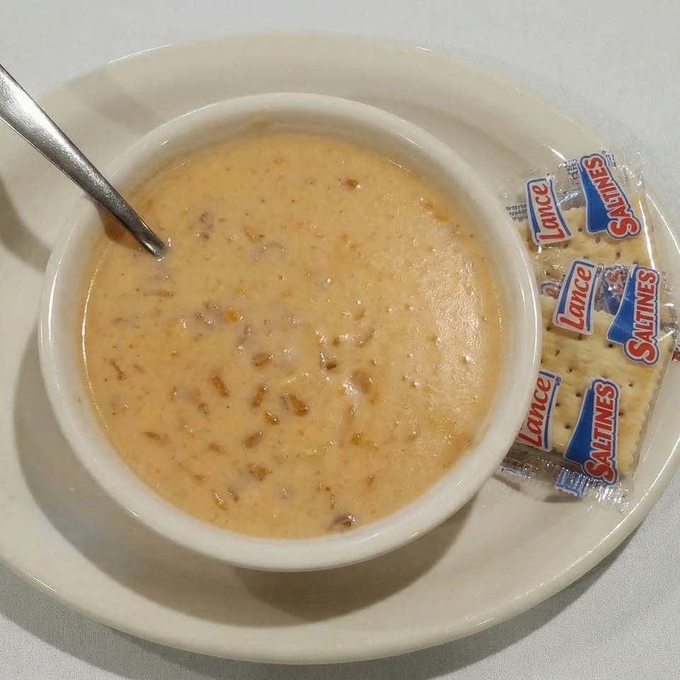 Creamy soup with a spoon in a white bowl, served with a packet of Lance Saltines.