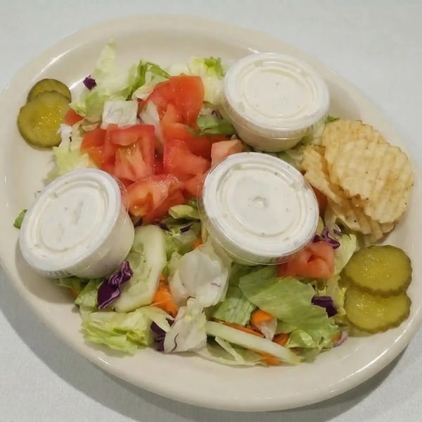 A side salad with lettuce, tomatoes, cucumbers, pickles, chips, and three ranch dressing cups.