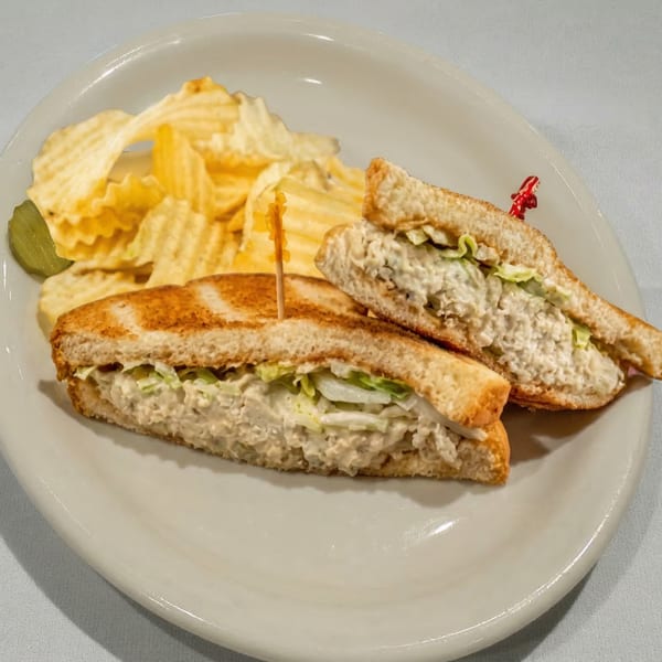 Toasted tuna salad sandwich with lettuce, served with crinkle-cut potato chips and a pickle.
