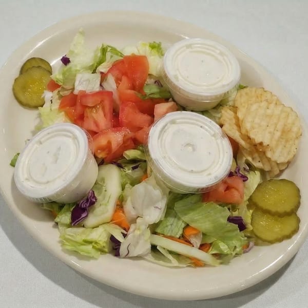 A side salad with lettuce, tomatoes, cucumbers, pickles, chips, and two ranch dressing cups.